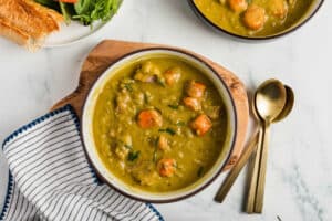 Slow Cooker Split Pea Soup in a bowl with spoons beside it.
