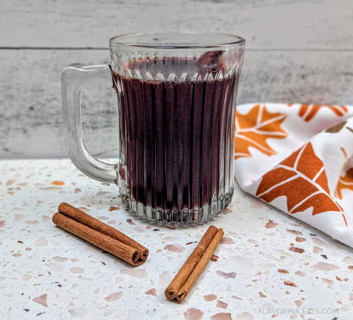 Slow Cooker Warm Apple Cinnamon Spiced Wine in a glass mug with cinnamon sticks beside it.