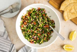 Middle Eastern Salad Shirazi served in a bowl with pita bread and lemons beside it.