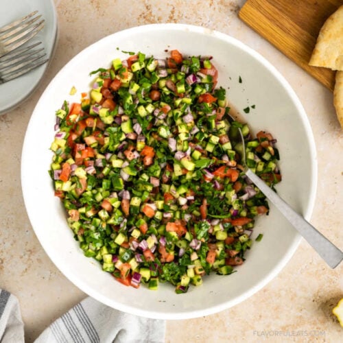 Middle Eastern Salad Shirazi served in a bowl with pita bread and lemons beside it.