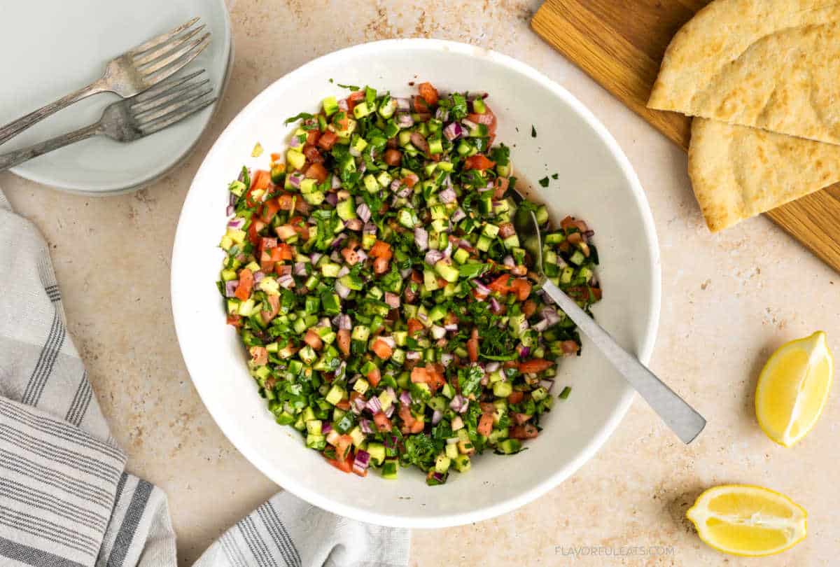 Middle Eastern Salad Shirazi served in a bowl with pita bread and lemons beside it.