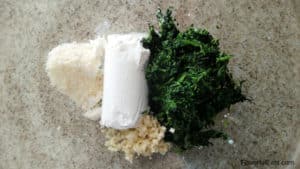 A glass bowl with the garlic, spinach, goat cheese, and parmesan cheese in it before it's mixed together.