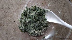 A glass bowl with the spinach, garlic, goat cheese, and parmesan cheese all mixed together to stuff the chicken.