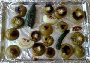 Tomatillos, onion, and peppers on baking sheet after they've roasted. They have charred marks.