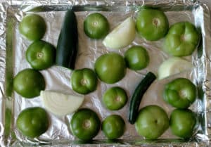 Tomatillos, onion, and peppers on baking sheet before they're roasted.