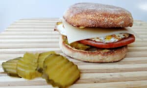 Cuban Breakfast Sandwich on a cutting board with sliced pickles beside it.