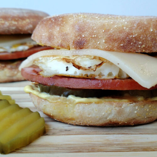 Cuban Breakfast Sandwiches on a cutting board with pickles beside them.