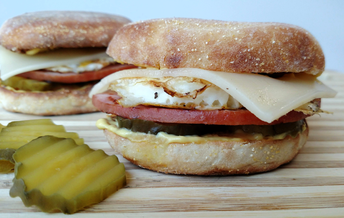 Cuban Breakfast Sandwiches on a cutting board with pickles beside them.