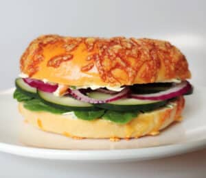 Garlic & Scallion Cream Cheese Spread on a bagel sandwich with fresh vegetables.
