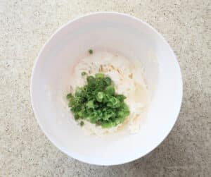 A mixing bowl with cream cheese, sliced scallions, and garlic powder, ready to make Garlic & Scallion Cream Cheese Spread