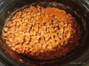 Slow cooker with cooked refried beans before they're blended smooth.