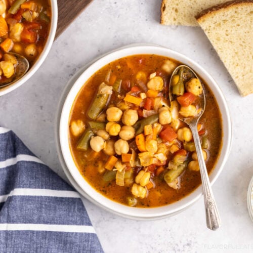 Bowls of Italian Chickpea Vegetable Soup with bread and parmesan beside them.