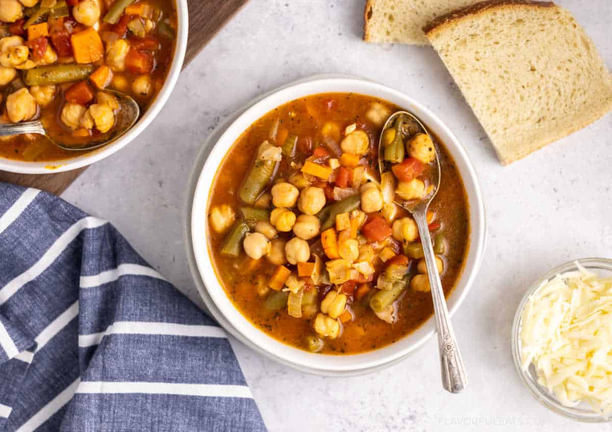 Bowls of Italian Chickpea Vegetable Soup with bread and parmesan beside them.