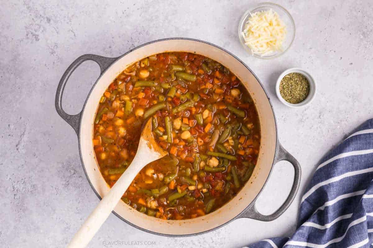 Italian Chickpea Vegetable Soup in the pot with cheese and herbs in little bowls beside it.