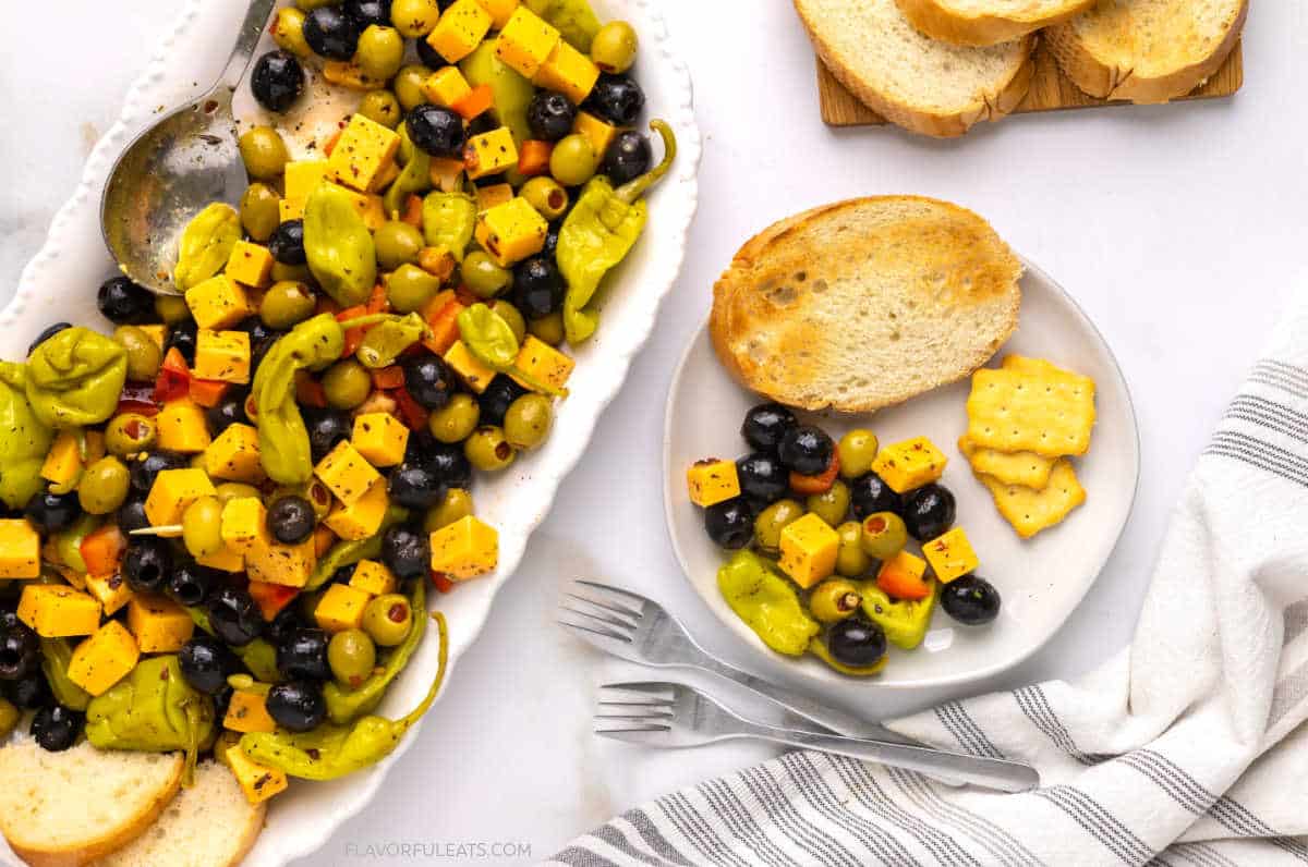 Marinated Cheese & Olive Antipasto on a platter with a small plate of the antipasto with bread and crackers on it.