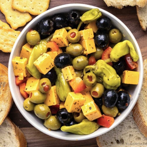 Marinated Cheese & Olive Antipasto in a bowl with bread and crackers beside it.