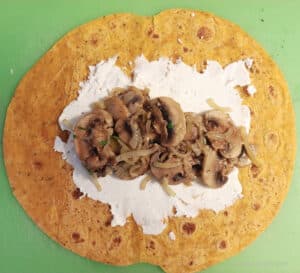A wrap with goat cheese spread on it topped with sauteed mushrooms.