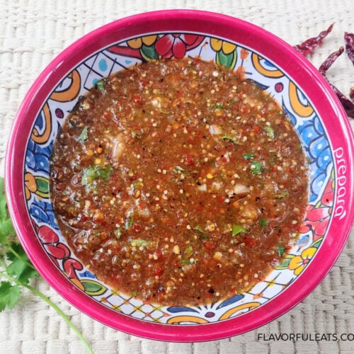 Chile de Arbol Tomatillo Salsa in a colorful bowl with cilantro and chile de arbol beside it.