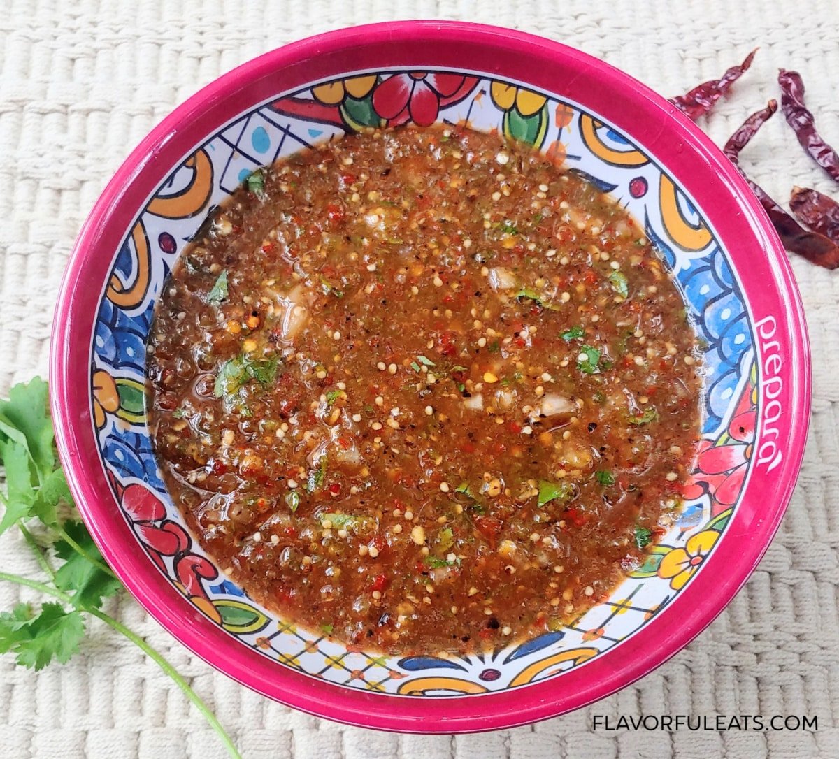 Chile de Arbol Tomatillo Salsa in a colorful bowl with cilantro and chile de arbol beside it.