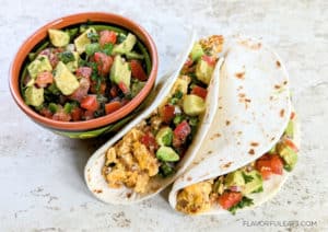 Two Chorizo Breakfast Tacos with a bowl of avocado pico de gallo next to them.
