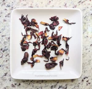 A square white plate with dried hibiscus flowers on it.