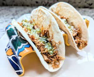 Tacos filled with the Slow Cooker Chipotle Chicken, topped with cheese and salsa verde.