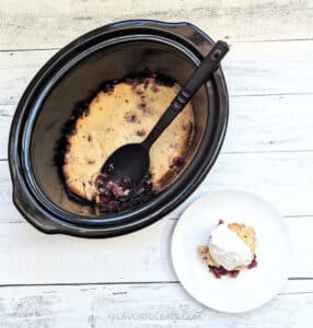 Slow Cooker Cranberry Cobbler in the slow cooker with a serving beside it on a white plate.