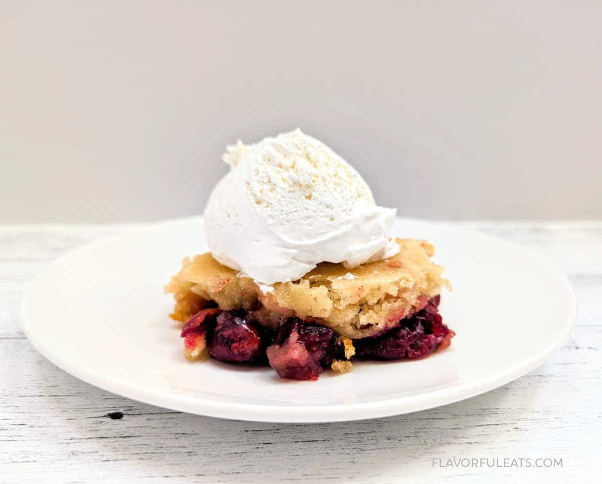 A serving of Slow Cooker Cranberry Cobbler on a plate with whipped cream on top.