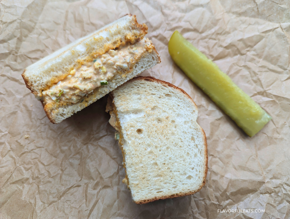 Cajun Egg Salad in a sandwich with a pickle on the side