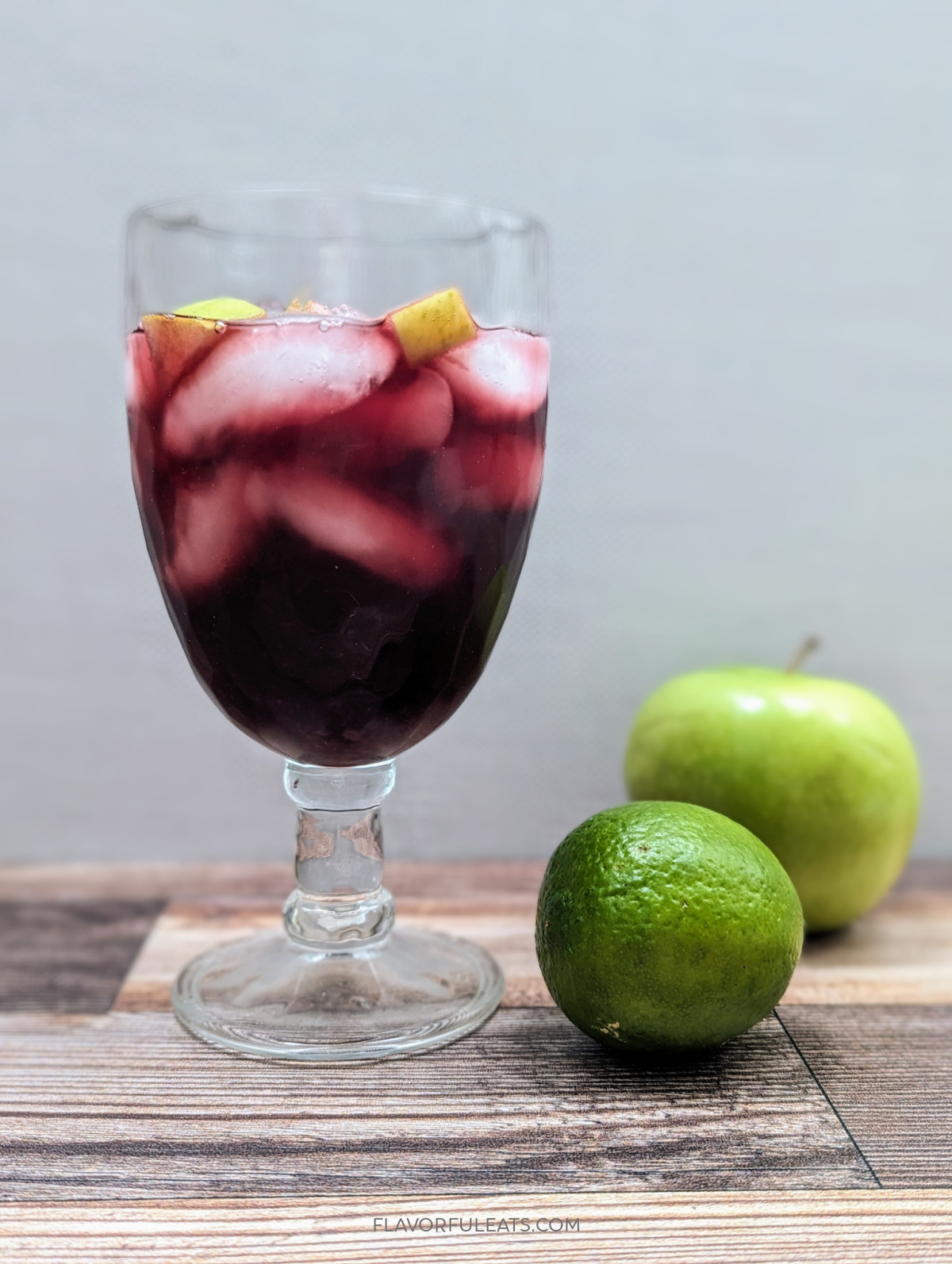 A goblet filled with Blackberry Moonshine Sangria and an apple and lime next to it.