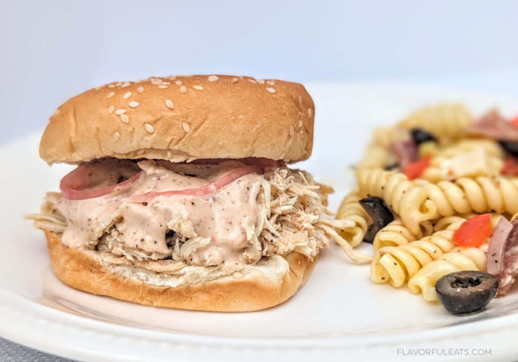 Slow Cooker Chicken Sandwich with Alabama White Sauce on a plate with pasta salad