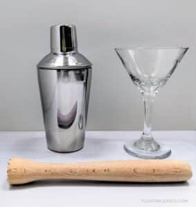The equipment needed to make a Hawaiian Smash Martini - shaker, martini glass, muddler, and mesh strainer.