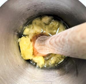 The inside of a cocktail shaker showing a muddler smashing lemon and pineapple