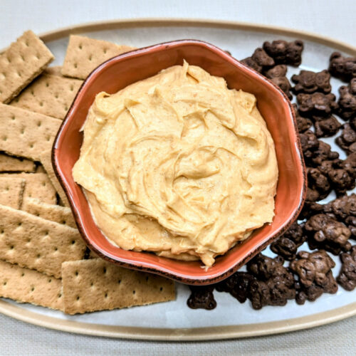 Pumpkin Cheesecake Dip in a bowl with Graham crackers and chocolate Teddy Grahams beside it on a tray