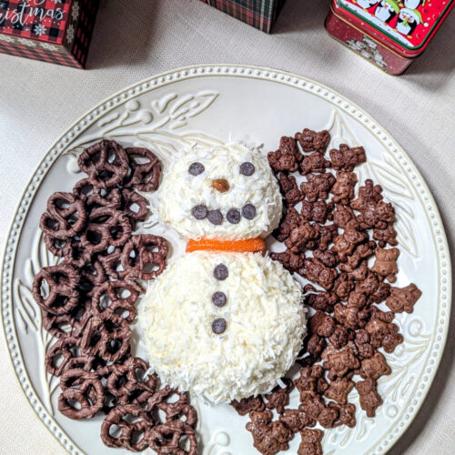 Coconut Snowman Cheese Ball on a large white platter with things to dip in it. There are festive gift boxes near it.