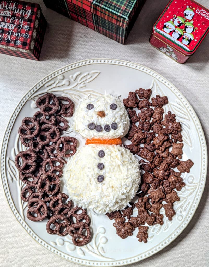 Coconut Snowman Cheese Ball on a large white platter with things to dip in it. There are festive gift boxes near it.