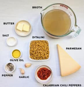 A photo of all the ingredients needed to make Calabrian Chili Butter Ditalini Pasta (One-Pan Recipe). It shows broth, butter, ditalini pasta, parmesan, Calabrian chili peppers, olive oil, garlic, salt, and pepper.