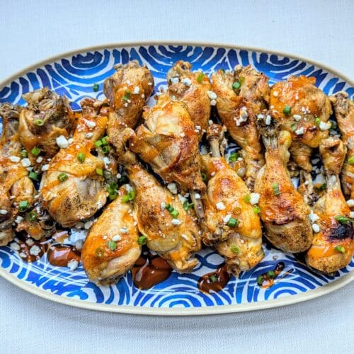 A blue platter with Slow Cooker Buffalo Chicken Drumsticks stacked on it with sliced scallions and blue cheese crumbles garnished on top.
