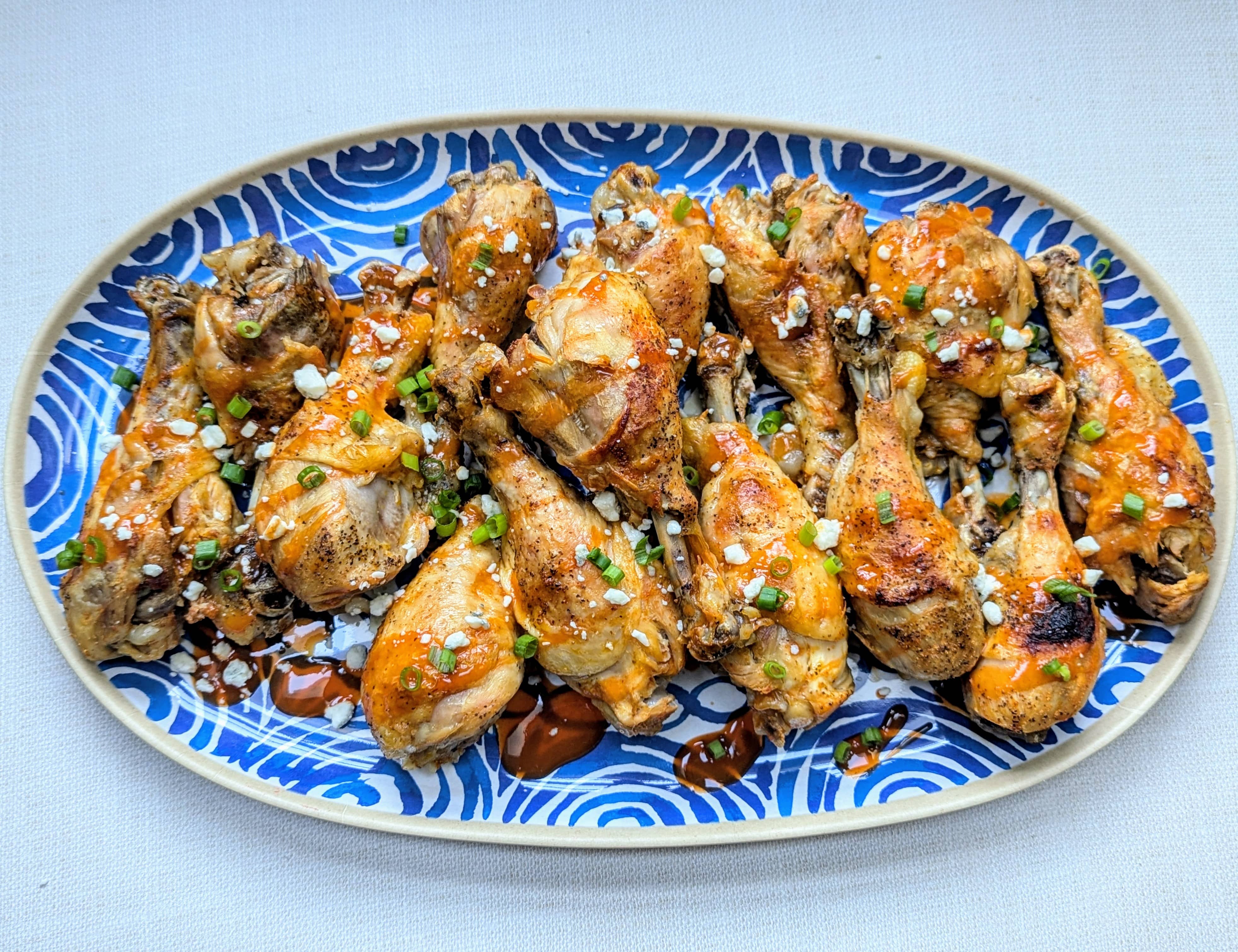 A blue platter with Slow Cooker Buffalo Chicken Drumsticks stacked on it with sliced scallions and blue cheese crumbles garnished on top.
