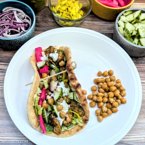 Sheet Pan Za'atar Chicken & Chickpeas in a flatbread with a variety of toppings in the background.