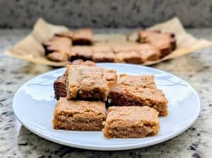 Slow Cooker Peanut Butter Cookie Bars stacked on a plate with more on parchment paper in the background