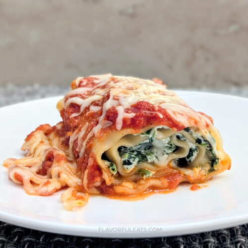 A close-up of a Cheesy Spinach Lasagna Roll Up on a white plate.