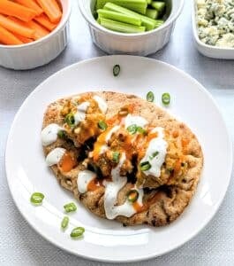 Baked Buffalo Chicken Meatballs on a plate with naan with bowls of carrots, celery, and blue cheese crumbles beside it.
