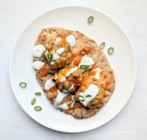Baked Buffalo Chicken Meatballs on a naan with condiments drizzled over them.