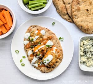 Baked Buffalo Chicken Meatballs on flatbread with ranch and blue cheese crumbles with carrots, celery, and flatbread beside it.
