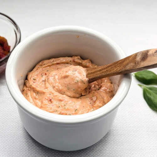 A small white bowl filled with Roasted Garlic Sun-Dried Tomato Aioli with a spoon in it.