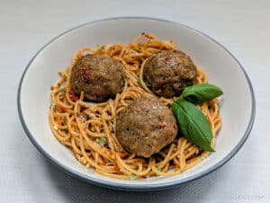 Baked Sun-Dried Tomato Turkey Meatballs in a bowl with spaghetti.