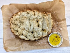 Slow Cooker Herbed Focaccia Bread on parchment paper with a small dish of seasoning olive oil beside it for dipping.