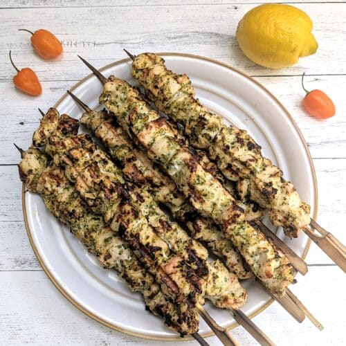 Grilled Habanero Marinated Chicken Skewers on a white plate with lemon and habaneros beside it.
