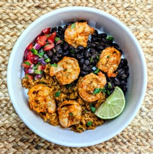 Achiote Shrimp Skewers in a white bowl with Mexican rice, black beans, and pico de gallo.